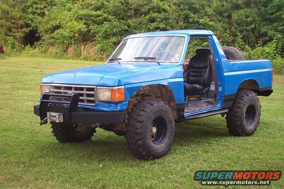 Blue lifted pickup truck with off-road tires and a winch on the front bumper. The driver's side door is open, showing black leather seats