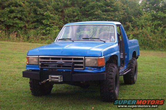 Blue Ford Bronco with large tires, aftermarket bumper, and winch. Driver's door is open