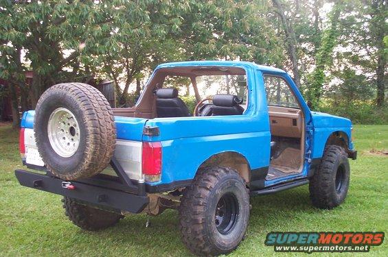 Blue 1987 Ford Bronco with spare tire on rear bumper and aftermarket sliders