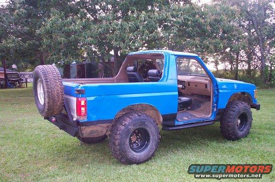 1987 Ford Bronco, blue, with spare tire mounted on rear bumper, doors open, off-road tires