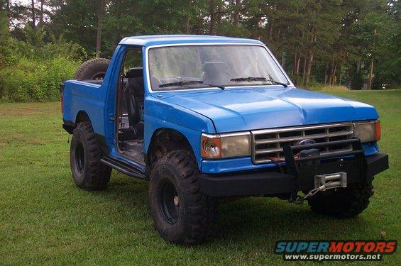 Blue off-road truck with winch and spare tire on back. Driver's door is open