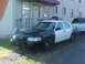 1999 Ford Crown Victoria - A two-tone police car is parked next to a building with another vehicle behind it.