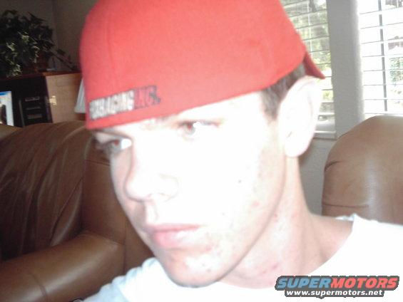 Man wearing a red baseball cap with text, sitting on a brown leather couch