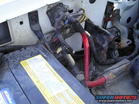 Engine bay with battery, wiring, and alternator components. Some rust is visible on metal brackets