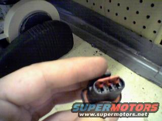 Hand holding a black and orange electrical connector with three pins
