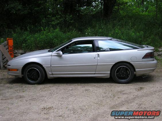 1990 Ford Probe coupe, side view, parked on dirt road with trees in background