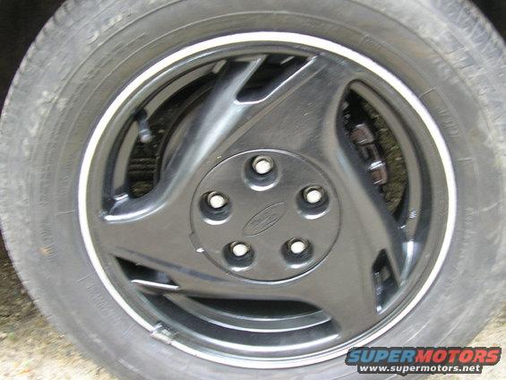 Close-up of a black car wheel with a Ford logo on the hubcap. Tire has a white stripe