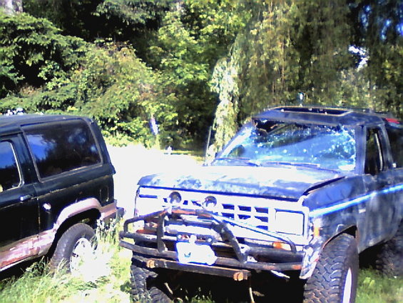 Dark blue SUV with a damaged windshield and a brush guard, parked next to a dark green SUV
