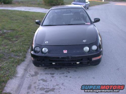 Front view of a black coupe with a red Honda badge. Another car is visible in the background
