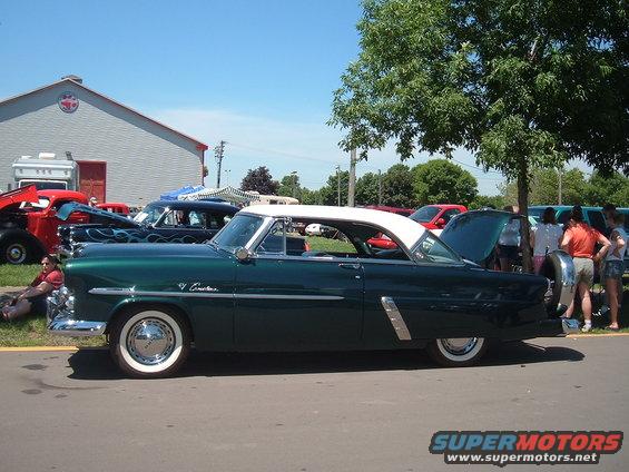Green 1955 Ford Fairlane Crown Victoria with white roof, parked next to other cars