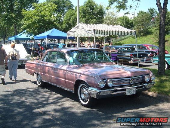 Pink sedan with chrome grille and dual headlights parked at an outdoor car show