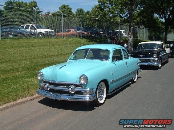 Light blue 1950 Ford sedan with whitewall tires parked on a street, other classic cars behind it