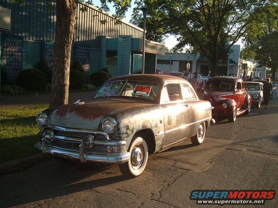 Rusty 1950 Ford Custom sedan with a "For Sale" sign in the windshield, parked on a street