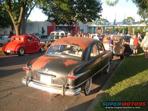 Rear view of a weathered black and red sedan with whitewall tires