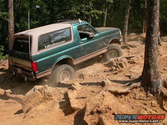 Green Ford Bronco climbing rocky terrain, tan top, off-road tires