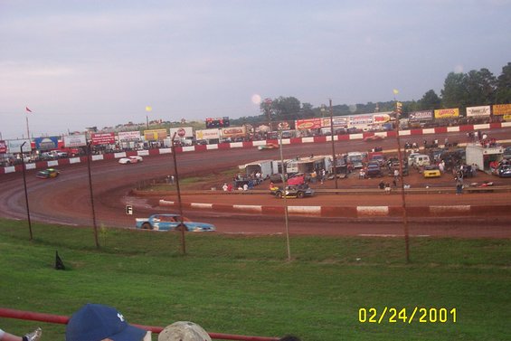 Dirt racetrack with several race cars on the track and parked in the background