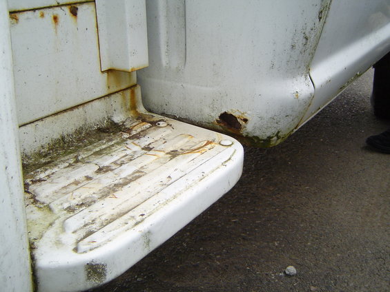 Close-up of a white truck's rear step and fender, showing rust and dirt