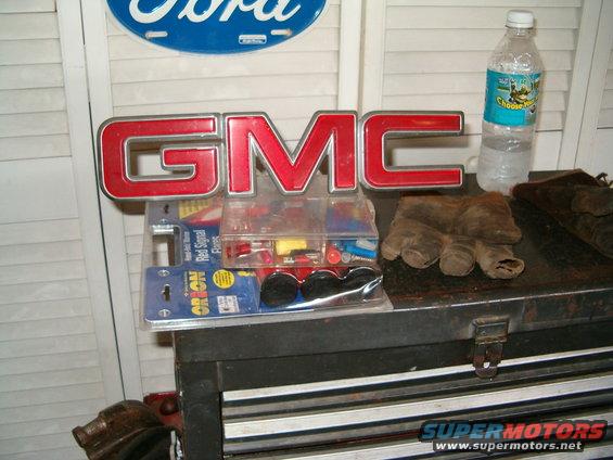 GMC emblem, gloves, and assorted automotive parts on a toolbox. A Ford sign is visible in the background