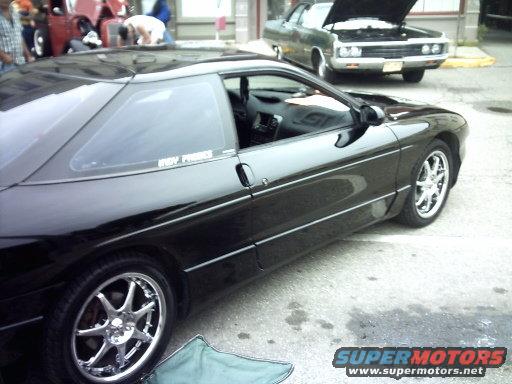 Black sports coupe with aftermarket wheels. Another car with hood up is parked behind it