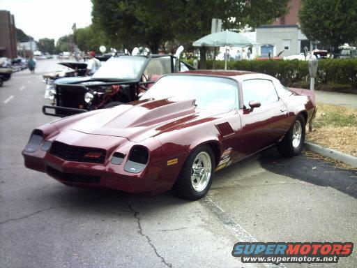 maroon Chevrolet Camaro with a hood scoop parked on a street, another vehicle with its hood up behind it