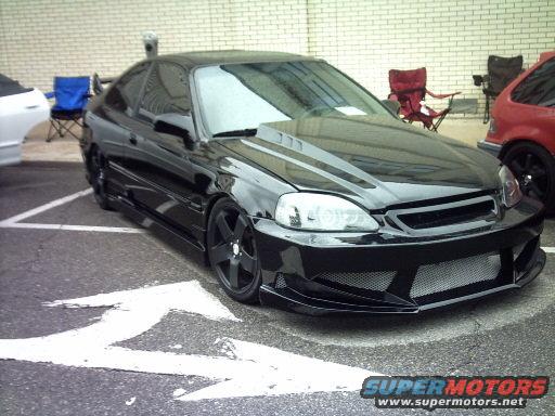 Black coupe with aftermarket body kit and hood scoop, parked in a lot