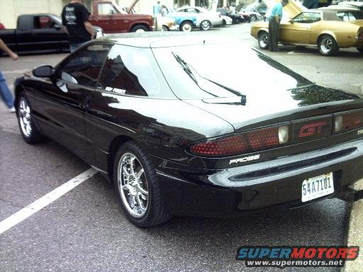 Black Ford Probe GT with chrome wheels parked on a street. Other cars and people are visible in the background