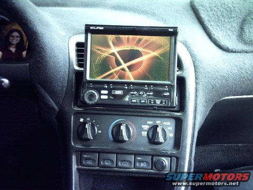 Car interior showing dashboard with an aftermarket Eclipse stereo and climate controls. A person is reflected in the driver's side mirror