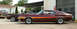 1972 Ford Torino - Two maroon Ford Torinos are parked in front of a building, with a red pickup truck on a trailer visible in the background.