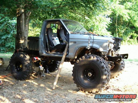 Modified pickup truck with oversized tires, missing front end components, and open doors