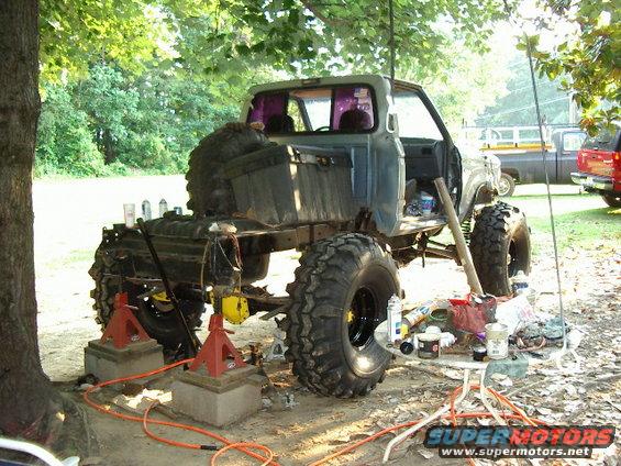 Pickup truck on jacks with big tires, parts scattered around. Another truck in background