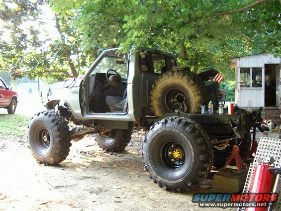 Modified pickup truck with oversized tires, missing doors, and a spare tire mounted on the rear