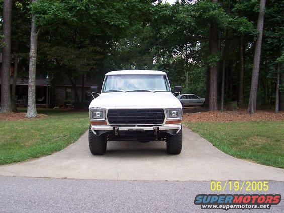 Front view of a white Ford truck with a black grille and aftermarket bumper. Another car is parked in the background
