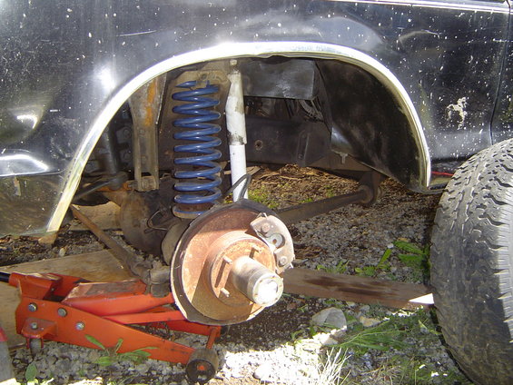 Close-up of a vehicle's rear suspension with blue springs and a jack underneath
