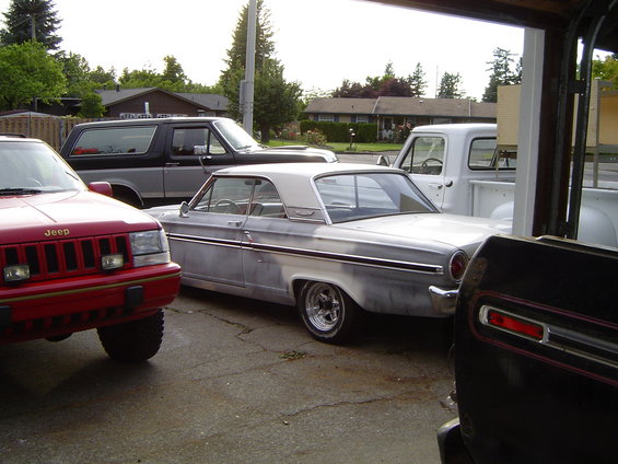 Red Jeep Cherokee, silver classic car, black Bronco, and white pickup truck parked outside