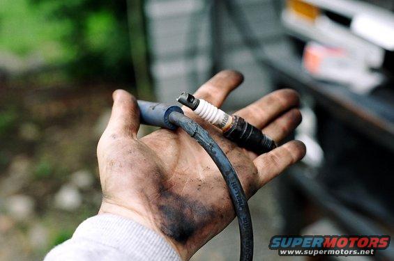 Dirty hand holding a spark plug and wire, with a SuperMotors logo in the corner