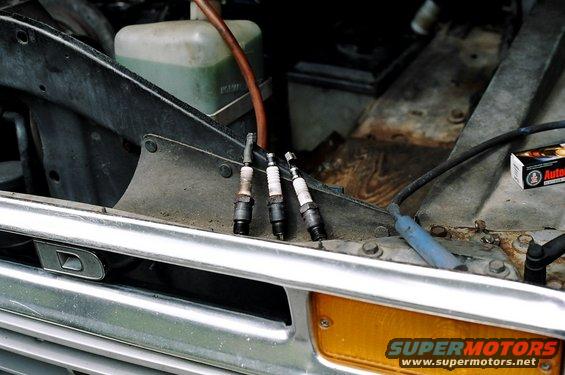1979 Ford Bronco engine bay with three spark plugs and a Supermotors.net logo
