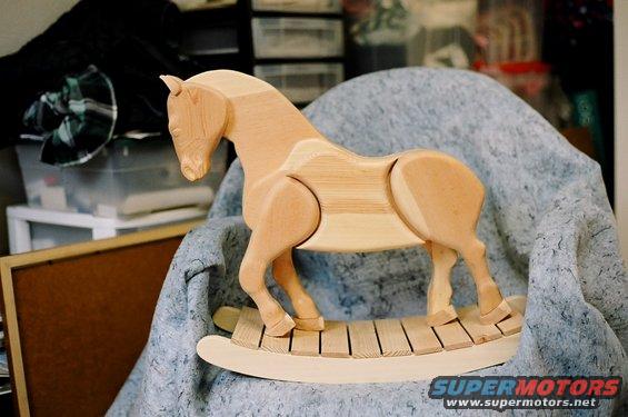 Unfinished wooden rocking horse on a chair with a blue blanket