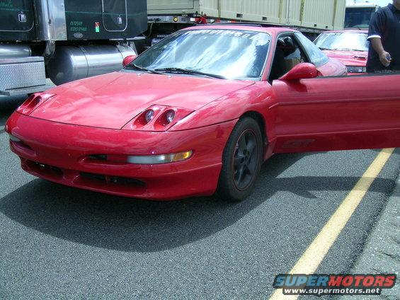 Red 1993 Ford Probe, driver's door open, parked next to a semi-truck