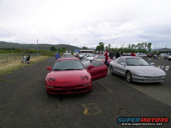 Red and silver Ford Probes parked on asphalt, with people around