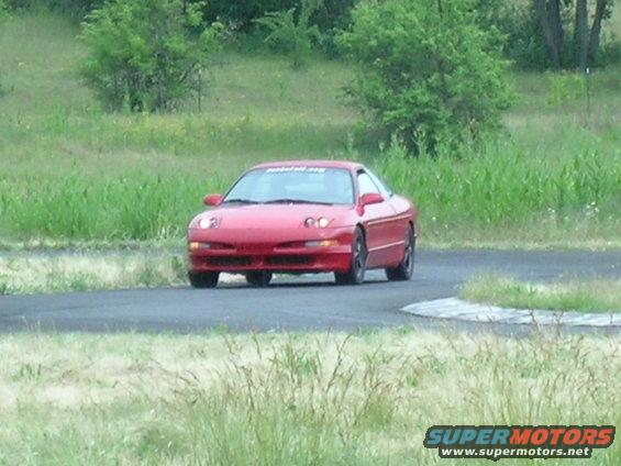 Red 1993 Ford Probe on a race track, front 3/4 view, with a banner on the windshield