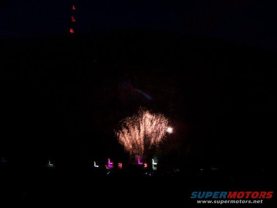 fireworks exploding in the night sky over a dark landscape with some distant lights