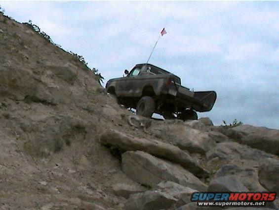 Truck with a flag on a pole going up a rocky incline