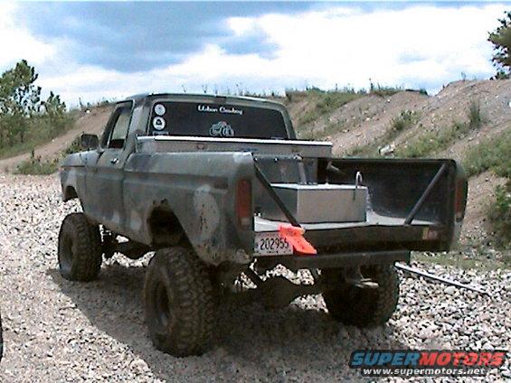 Gray 1977 Ford F-150 pickup truck with lifted suspension and aftermarket fuel tank in bed, rear view