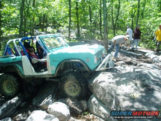 Light blue and white Ford Bronco navigating a rocky trail with people watching