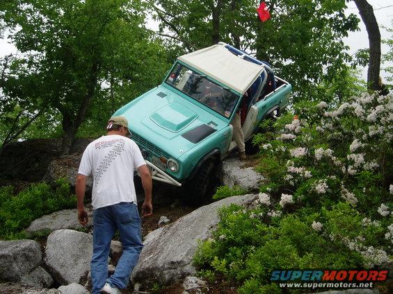 Teal Ford Bronco with white roof and roll cage navigating rocky terrain