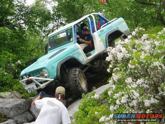1969 Ford Bronco climbing a rocky incline with a person guiding it