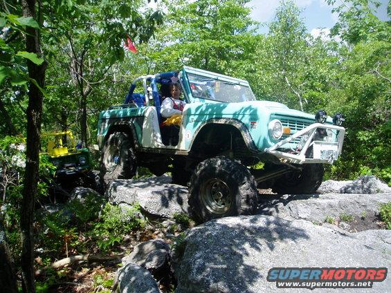light blue off-road vehicle with large tires navigating rocky terrain, another yellow vehicle behind it