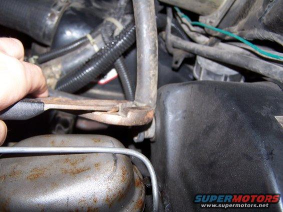 Hand holding pliers on a metal bracket in a vehicle's engine bay