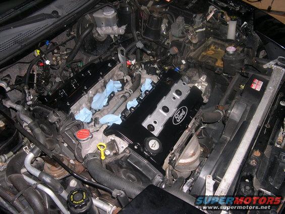 Close-up of a Ford engine with black valve covers and blue rags stuffed into openings. Radiator and hoses visible