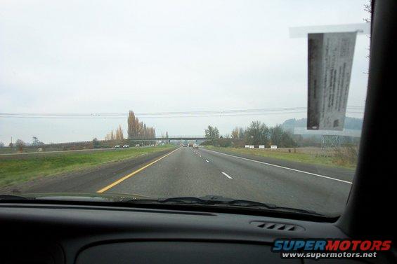 View from inside a car looking out at a highway with other cars visible in the distance and a sticker on the windshield